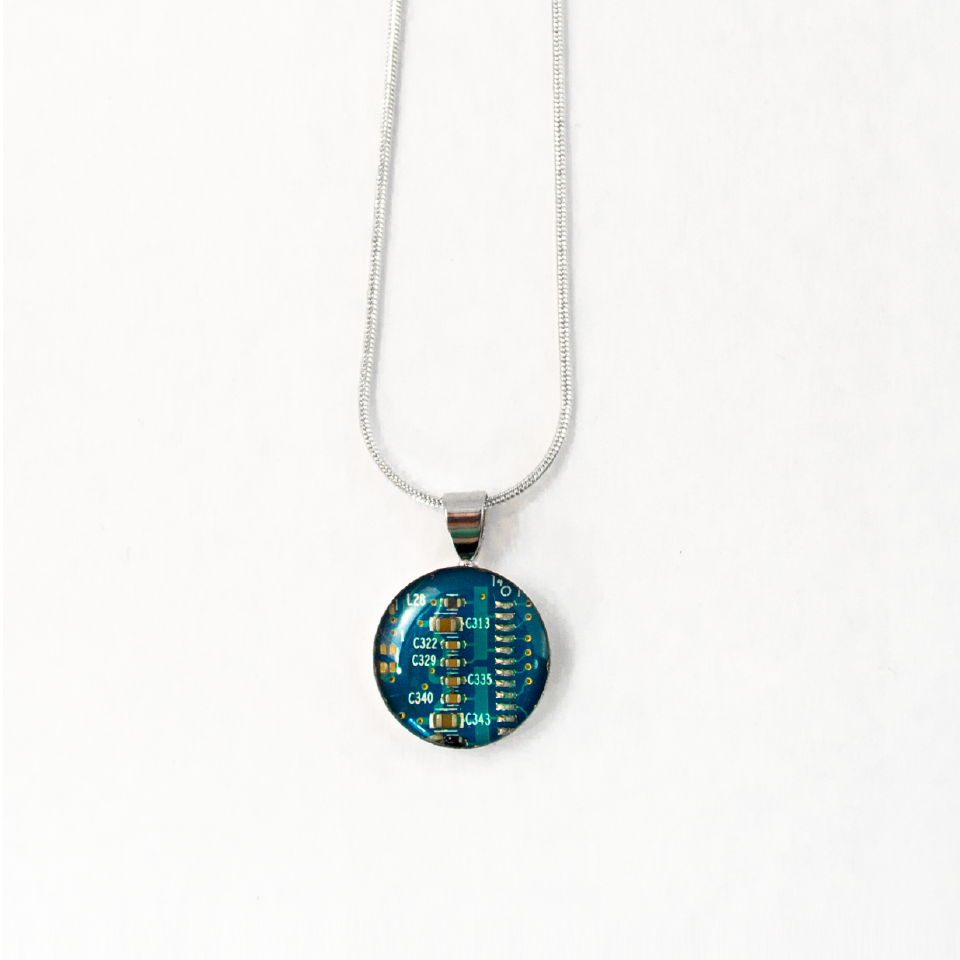 A small circular piece of circuit board is encased in a clear dome and hangs on a necklace chain