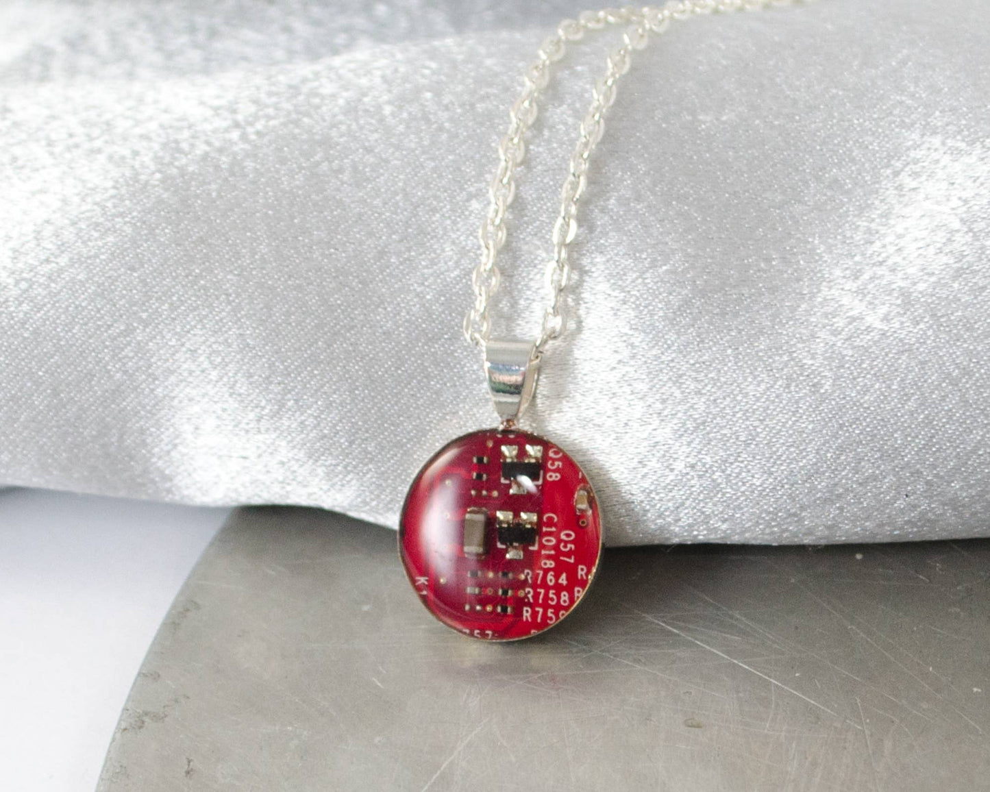 A piece of circuit board has been encased in clear resin and fixed into a circular pendant and hangs on a necklace chain