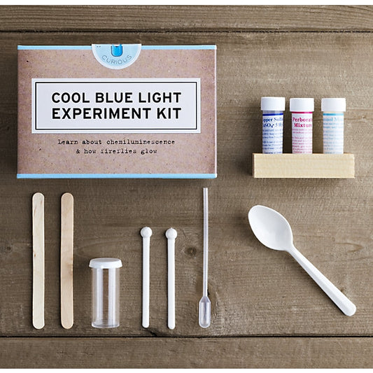 A brown box says "Cool Blue Light Experiment Kit"; items in kit are laid out including mixtures, spoon, pipette, and popsicle sticks
