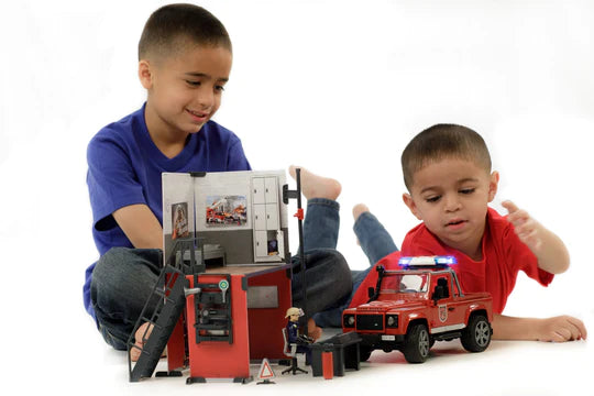 Two kids sit playing with model fire station and fire Land Rover