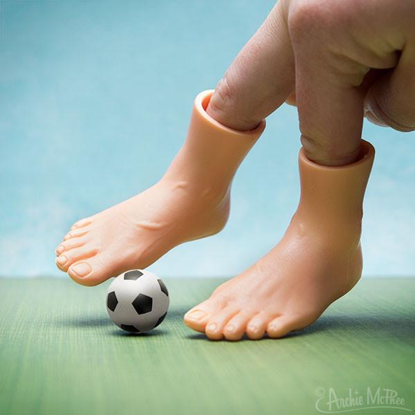 Finger-sized toy feet sit on hand, acting like they are going to "kick" a mini soccer ball