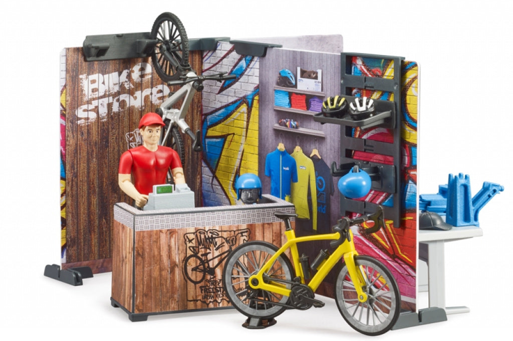 A man in a red shirt stands behind a cash register in a small bike store with a yellow bike in front and bike helmets on the shelves