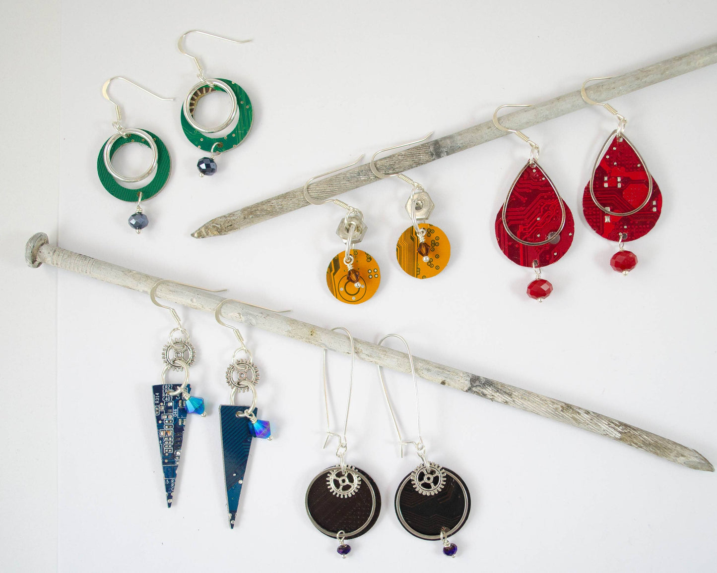 Different shapes of circuit board have been made into multi-colored earrings and are displayed on knitting needles